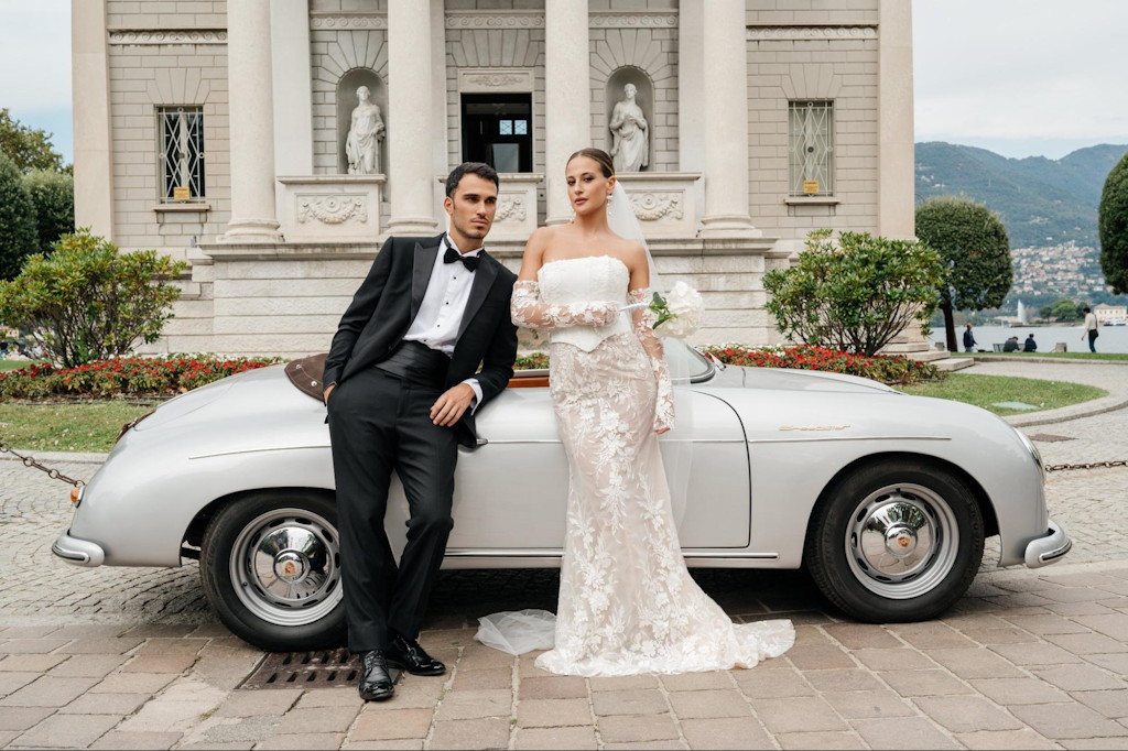 Elegantes Brautpaar posiert an einem silbernen Oldtimer-Cabrio vor einer Villa - filmreife Kulisse f&uuml;r den Hochzeitsfilm